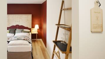 A bedroom with a wooden headboard, a bedside table with a lamp, and a wooden shelf with glassware.