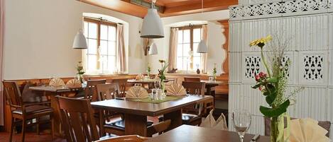 Un espace repas avec des tables et des chaises en bois, des luminaires suspendus et un vase décoratif rempli de fleurs.