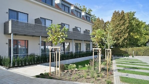 A modern building with a balcony, a garden with young trees, and a paved walkway. - Hotel & Restaurant Klosterhof (Gutenzell)