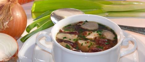 Un tazón de sopa con verduras y hierbas, rodeado de vegetales crudos como zanahorias, cebollas y ajo.