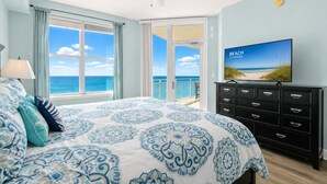 Un dormitorio con cama, cómoda, televisor y balcón con vista al océano.