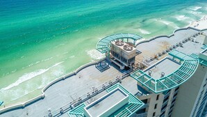 Vista aérea de un hotel costero con piscina en la azotea, una playa y un muelle al fondo.