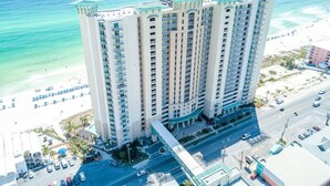 Un hotel moderno de altura con múltiples balcones, vistas a la playa y un estacionamiento.