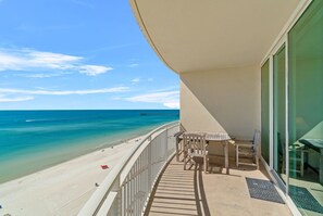 Un balcón con vistas a una playa y al océano, que incluye una mesa y sillas.