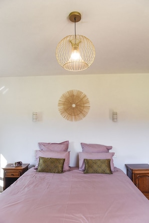 A bedroom with a bed, two bedside tables, a hanging light fixture, and a wall-mounted fan.