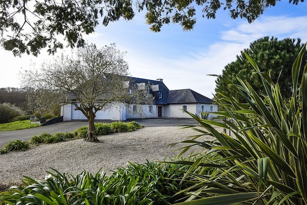 A two-story house with a gravel driveway and a tree in the foreground.