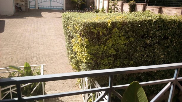 A paved courtyard with a hedge, a gated entrance, and a metal railing. - Kitui Premier Resort (Kitui)