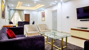 A modern living room with a glass coffee table, dark sofas, and a flat-screen TV. - Bella Residencia (Lekki)