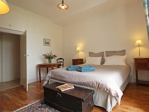 A bedroom with a bed, bedside tables, a wooden chest, and a small table with a vase of flowers.