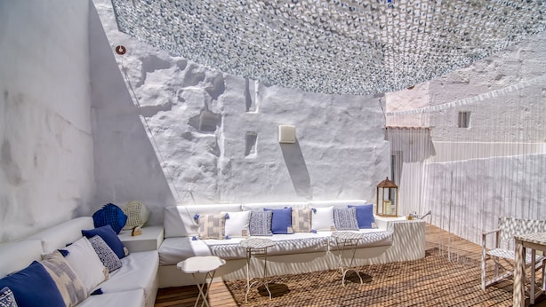A modern interior with a white sofa, patterned cushions, a wooden floor, and a unique ceiling design. - Hotel Ca s'Arader - Adults Only (Ciutadella de Menorca)