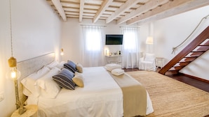 A bedroom with a large bed, wooden ceiling beams, a TV, a desk with a lamp, and a chair. - Hotel Ca s'Arader - Adults Only (Ciutadella de Menorca)