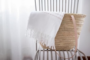 A woven basket with a strap, placed on a chair with vertical slats.