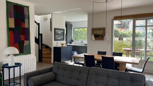 Ein modernes Wohnzimmer mit einem grauen Sofa, einem Esstisch mit Stühlen, einer Treppe und einem Küchenbereich.