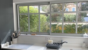 Eine moderne Küche mit einem großen Fenster, dunklen Schränken und einer weißen Arbeitsplatte.