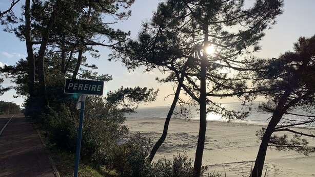 Eine Küstenstraße mit einem Schild, auf dem 'PEREIRE' steht, und einem Strand im Hintergrund.
