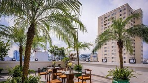 A rooftop terrace with outdoor seating, palm trees, and a view of a cityscape. - Triip Palago (Ho Chi Minh City)