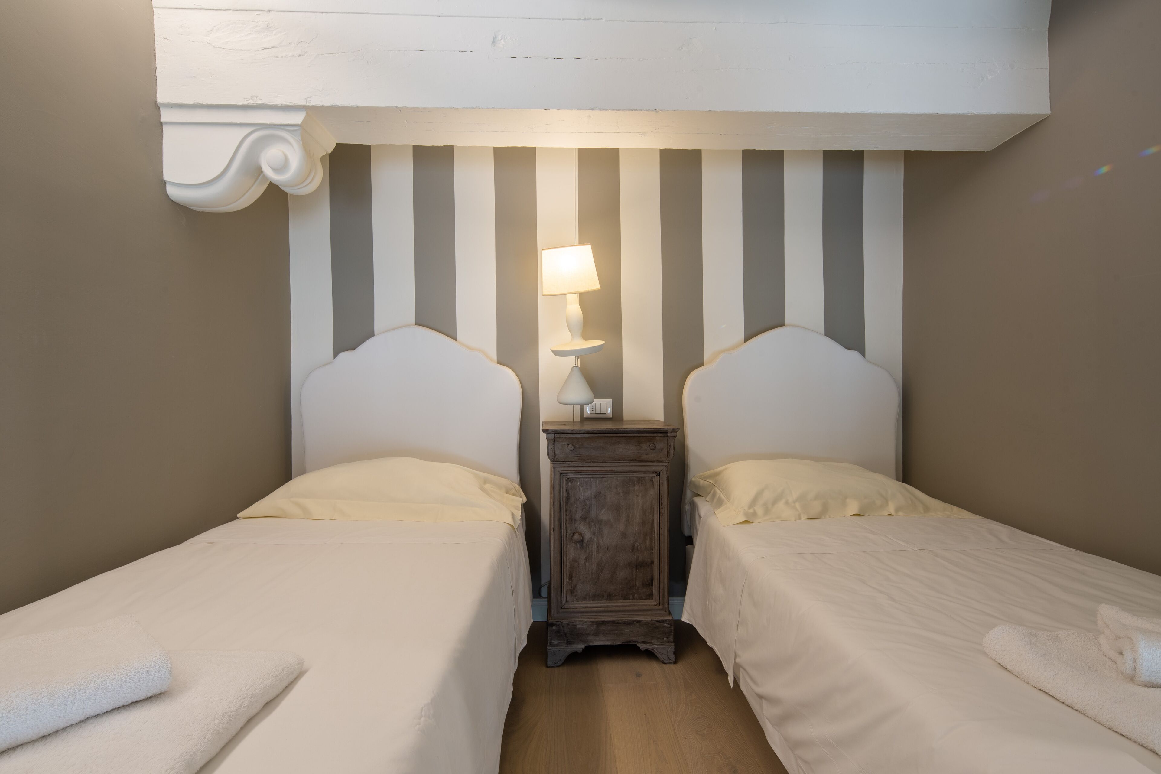 Una habitación con dos camas, una mesita de noche con lámpara y una pared a rayas.