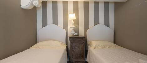 A room with two beds, a nightstand with a lamp, and a striped wall.