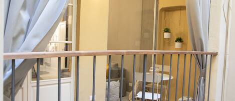 A balcony with a metal railing, a small table, and chairs. There are potted plants hanging on the wall.