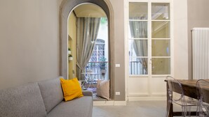 A living room with a grey sofa, a yellow pillow, a wooden table with transparent chairs, and a white door with glass panels. - Casa Velluti Deluxe by Mmega (Florence)