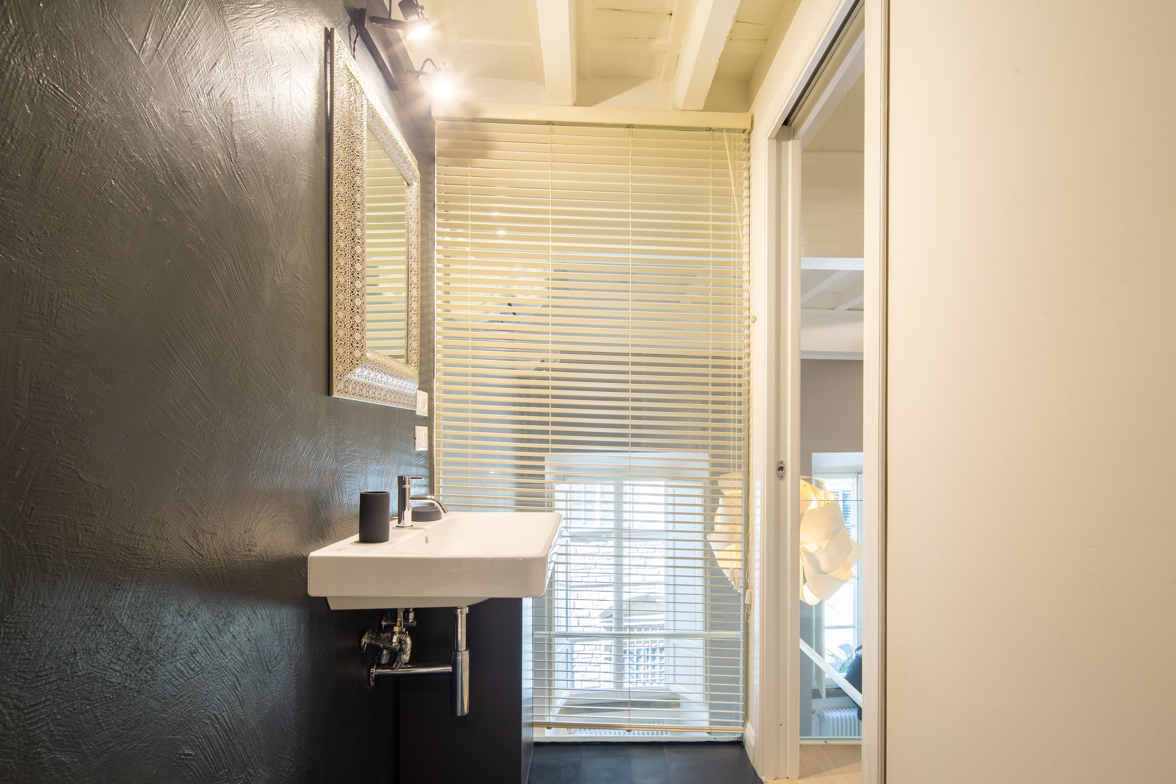 A bathroom with a white sink, a mirror, and a window with blinds.