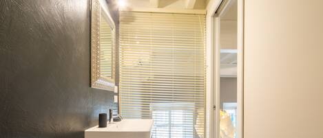 A bathroom with a white sink, a mirror, and a window with blinds.