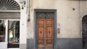 A double wooden door with a metal grid above it, set in a building with a beige and gray facade. - Casa Velluti Deluxe by Mmega (Florence)