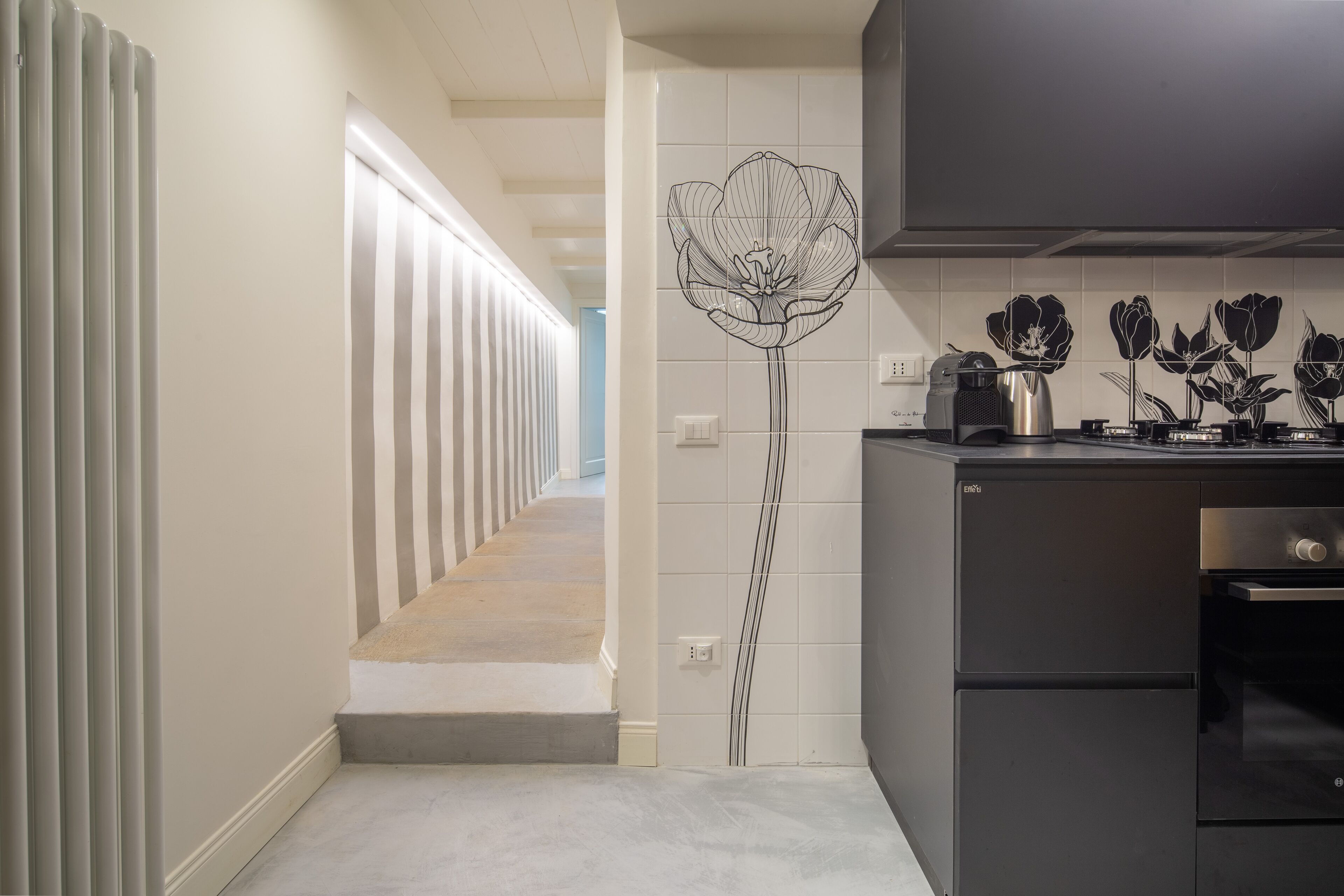 Een moderne keuken met een zwart aanrechtblad, roestvrijstalen apparatuur en een decoratieve wand met een bloemenmotief.