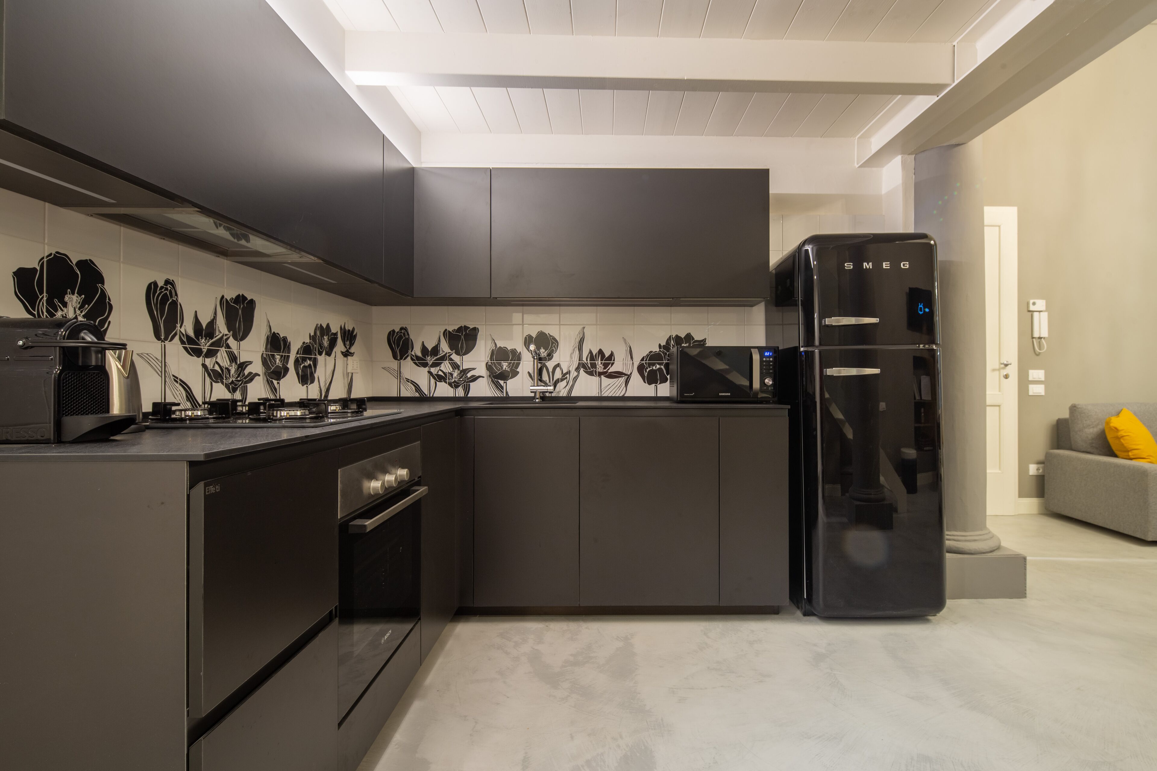 Una cocina moderna con armarios oscuros, un refrigerador negro y un salpicadero con diseños florales.