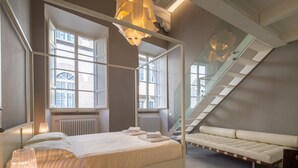 A modern bedroom with a four-poster bed, a sofa, large windows, and a staircase. - Casa Velluti Deluxe by Mmega (Florence)