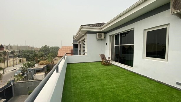 A modern building with a flat roof, large windows, and a green artificial lawn. - White Decor Penthouse (Lekki)
