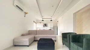 A modern living room with a sectional sofa, a black ottoman, and green armchairs. - White Decor Penthouse (Lekki)