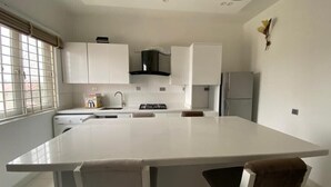A modern kitchen with white cabinetry, a central island, and a built-in stove. - White Decor Penthouse (Lekki)