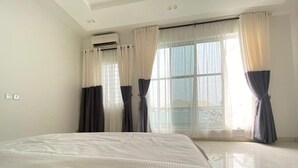 A hotel room with a large bed, air conditioning unit, and large windows with curtains. - White Decor Penthouse (Lekki)