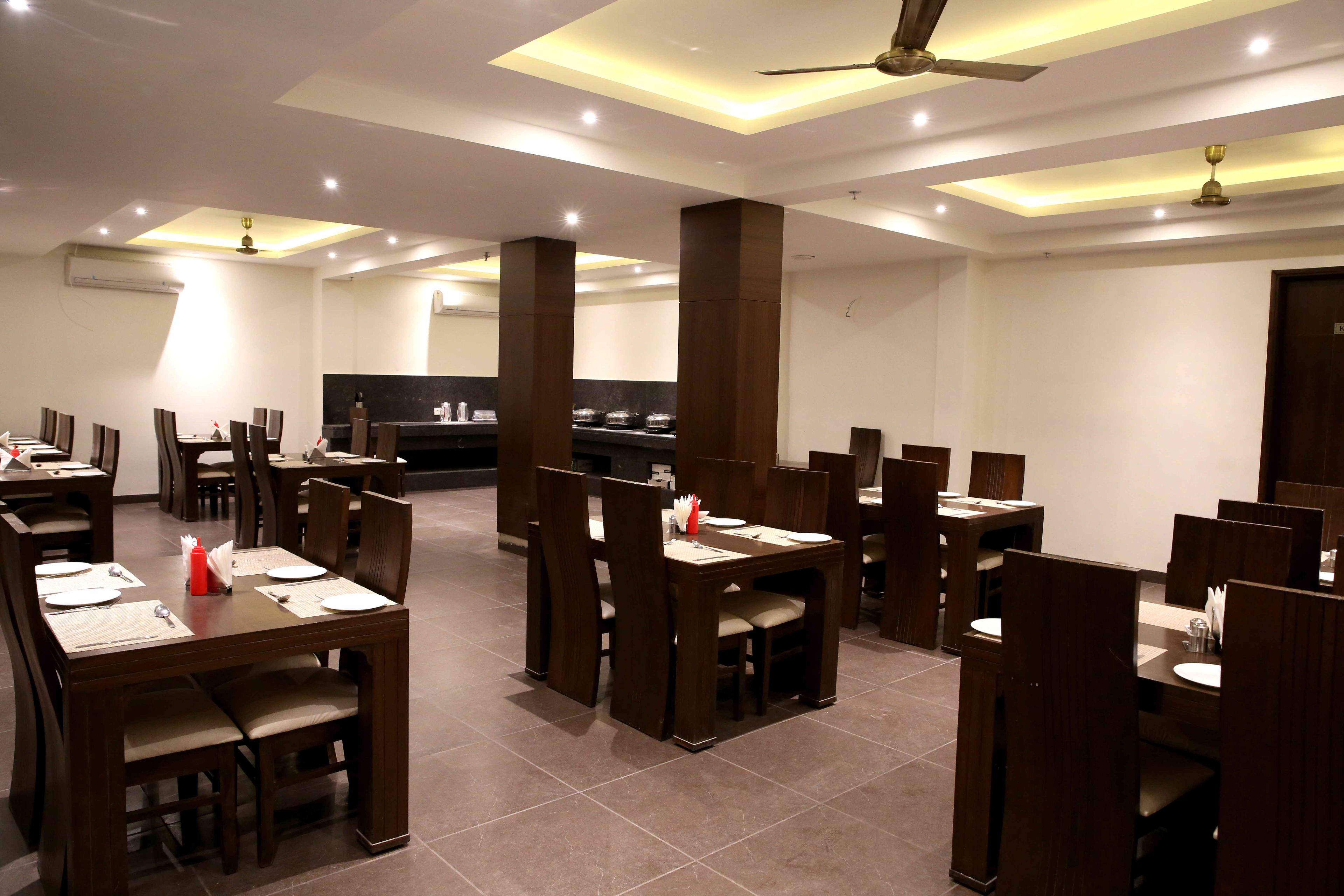 Restaurante com várias mesas e cabines para refeições, ventiladores de teto, iluminação embutida e uma área de cozinha ao fundo.