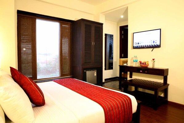 A hotel room with a bed, a television, a desk, and a view through a window.