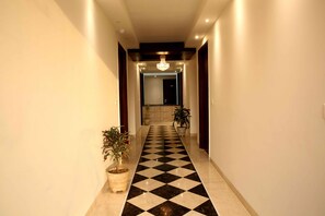 A hallway with a checkered floor, potted plants, and a chandelier. - The Raj Vilas (Agra)