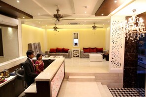A hotel lobby with a reception desk, seating area, and a chandelier. - The Raj Vilas (Agra)