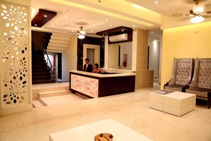 A modern hotel lobby with a reception desk, a staircase, and a seating area with two armchairs.