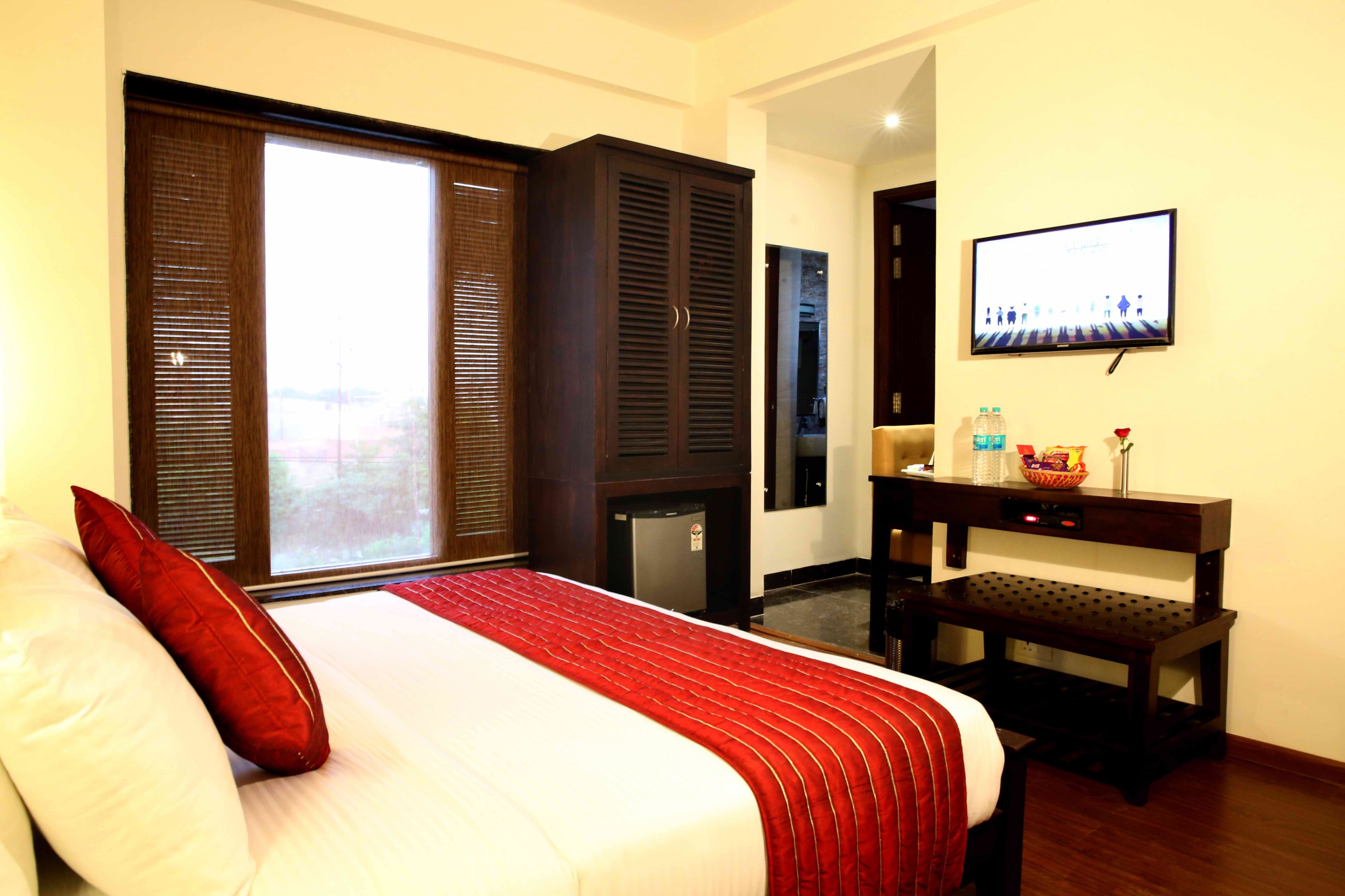 A hotel room with a bed, a television, a desk, and a view through a window.