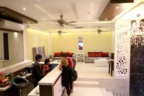 A hotel lobby with a reception desk, seating area, and a staircase leading to the upper floor. - The Raj Vilas (Agra)