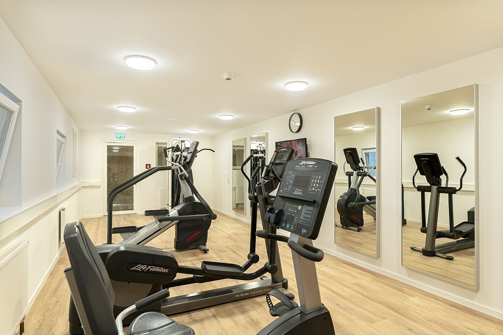 Un gimnasio con máquinas de cardio, espejos y suelo de madera.