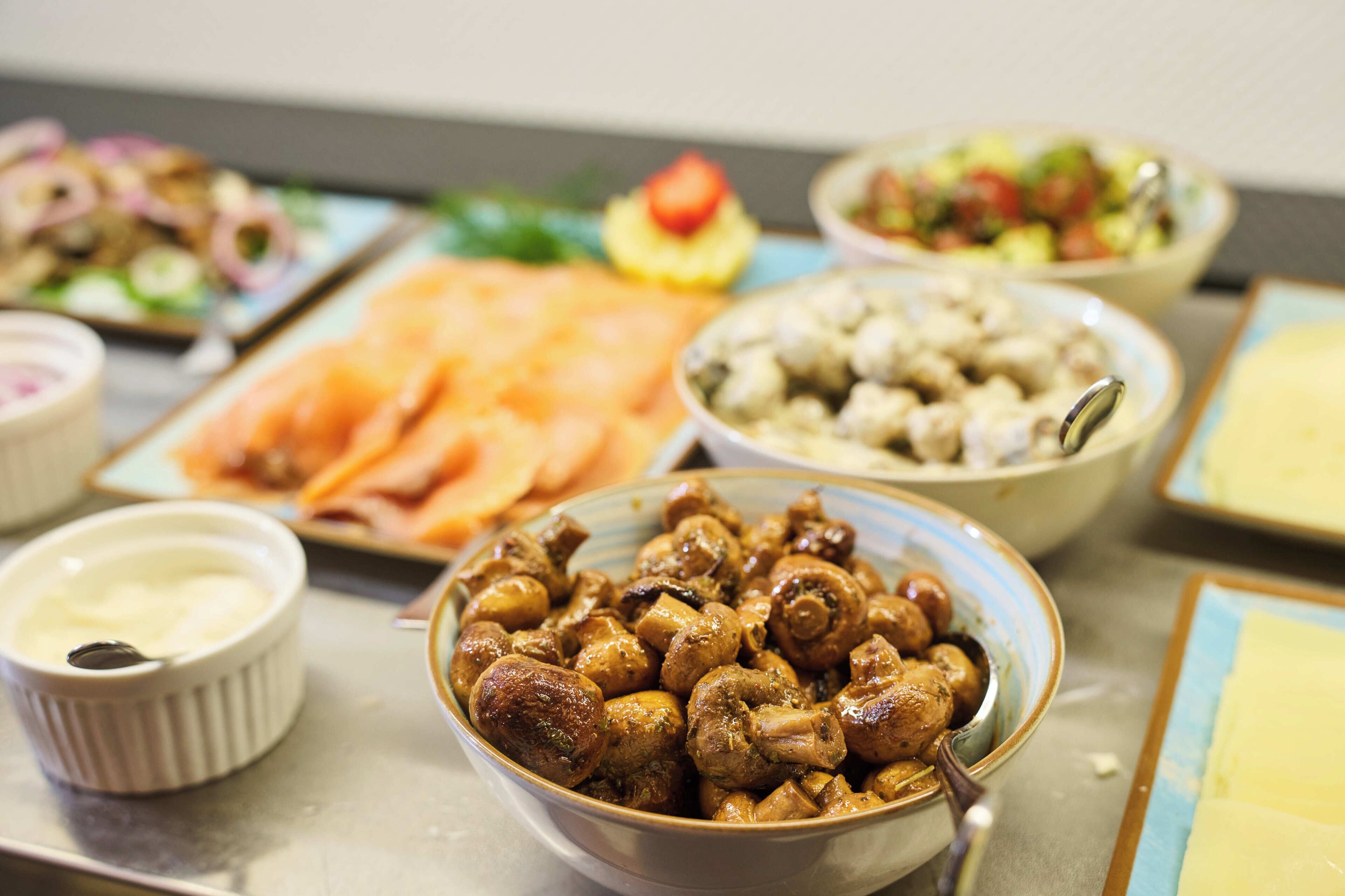 A buffet with various dishes including a bowl of mushrooms, a plate of salmon, and a salad.