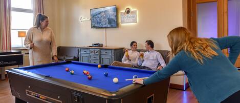 A pool table in a room with a cityscape TV, a sign reading "Benedikiner Wiesbräu," and a wooden cabinet.