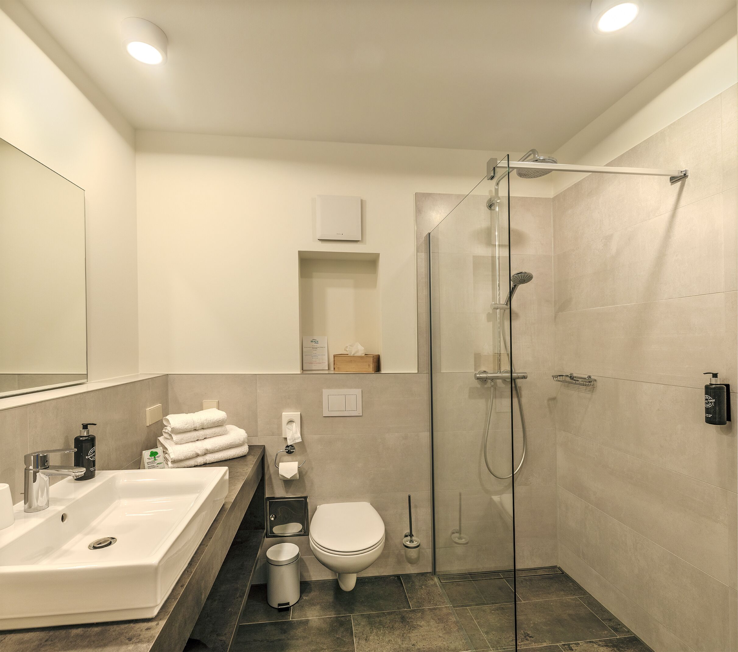 A modern bathroom with a glass-enclosed shower, a sink with a mirror, a toilet, and a towel rack.