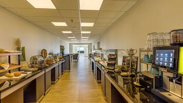 A long, well-lit kitchen area with multiple counters, coffee machines, and a display screen.