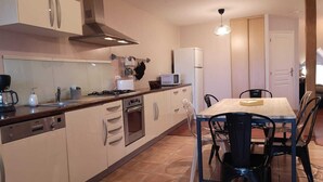 A compact kitchen with a stove, oven, and microwave. There is a dining table with chairs and a light fixture above it.