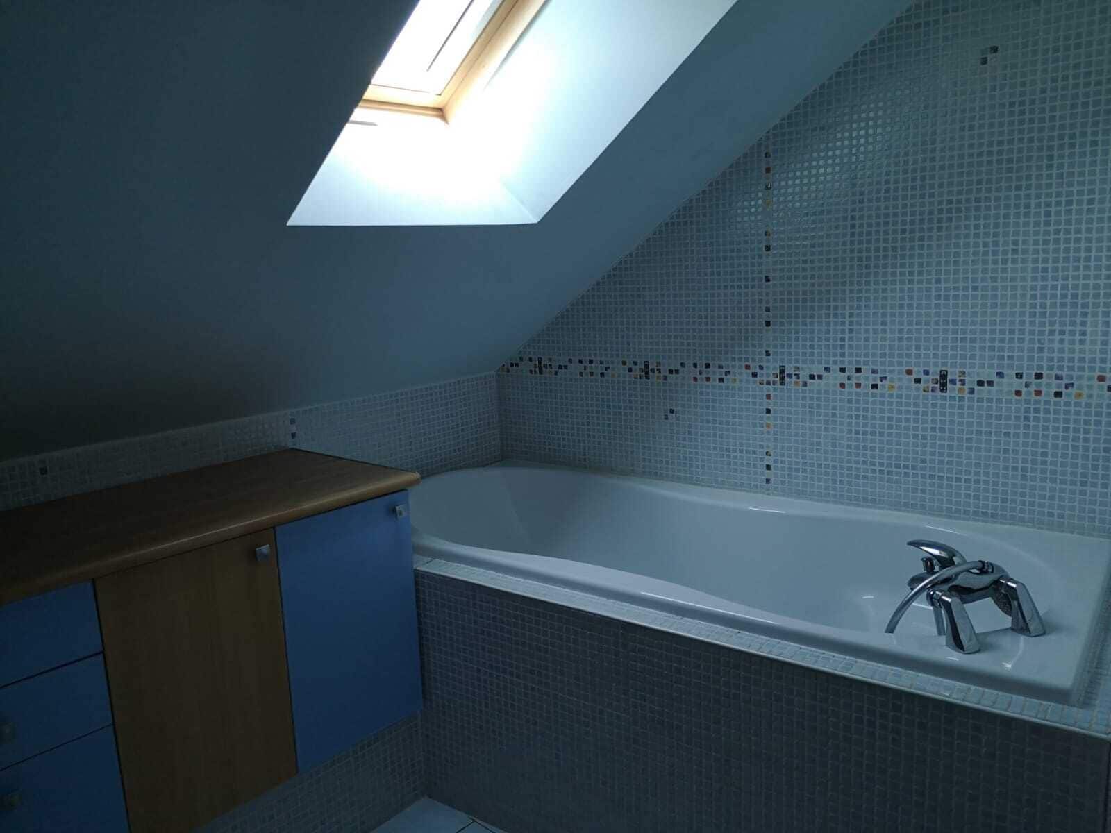 Un baño con tragaluz, bañera y un mueble azul.