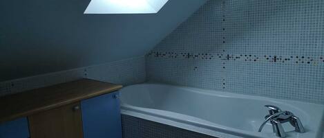 Un baño con tragaluz, bañera y un mueble azul.
