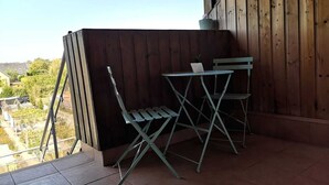 A balcony with a wooden wall, a small table with a laptop, two chairs, and a string of colorful lights.